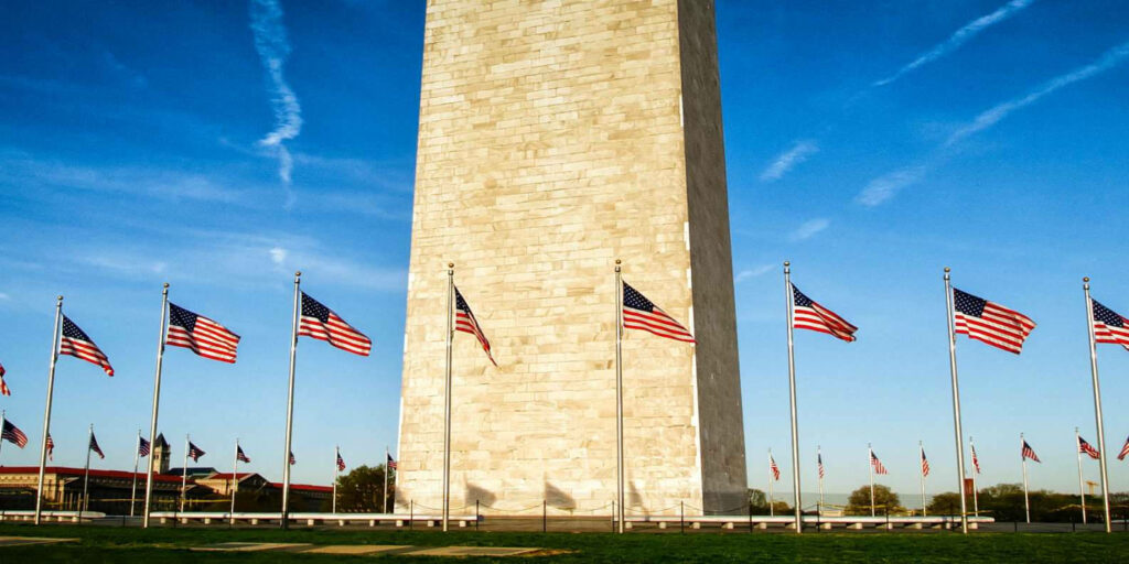 Washington Monument base surrounded by waving American flags under clear blue sky wallpaper