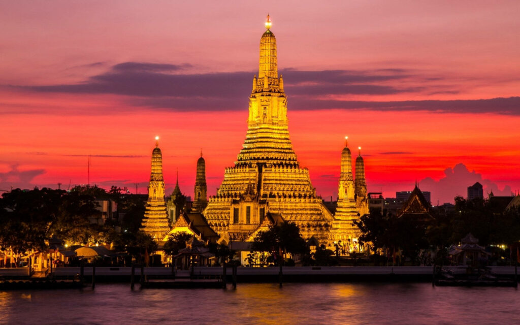 Wat Arun temple in Bangkok glowing at sunset with vibrant sky riverside iconic wallpaper background