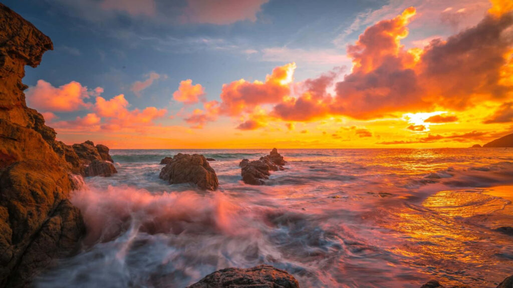 Spectacular Sunset Serenade: Majestic Waves Embrace Malibu Rocks in 1440p Beauty Wallpaper