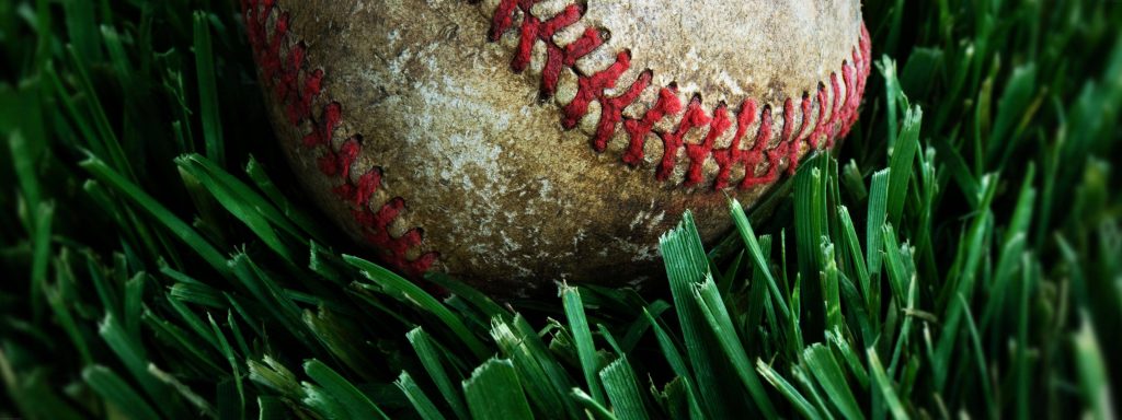 Weathered baseball with red stitching on vibrant green grass high contrast sports wallpaper