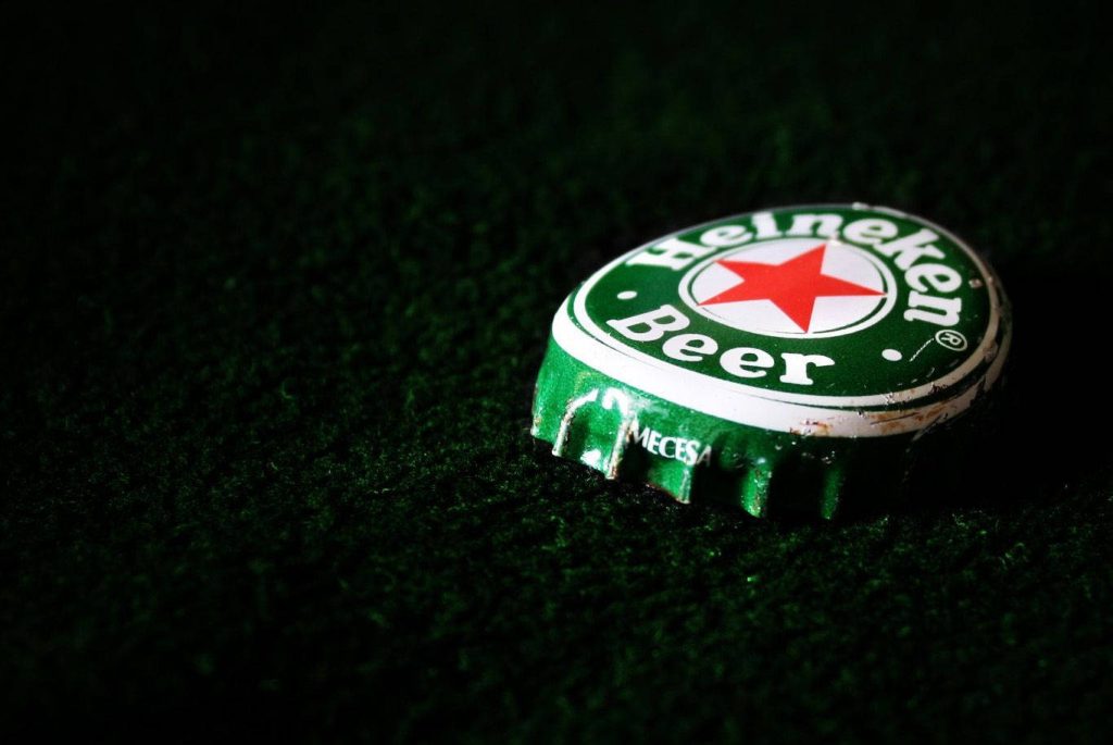 Close-up of weathered Heineken lager bottle cap on dark textured green surface wallpaper
