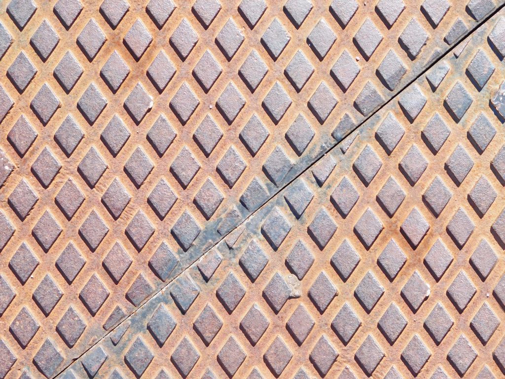 Weathered steel diamond plate texture with diagonal seam and rusted industrial gray pattern Wallpaper