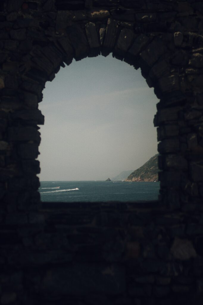 Weathered stone arch framing calm blue sea rugged coastline gentle waves soft hazy sky wallpaper