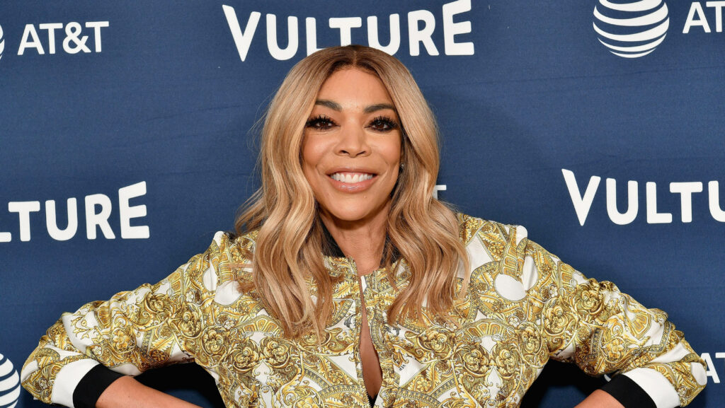 Wendy Williams smiling confidently in patterned jacket at Vulture event with wallpaper backdrop