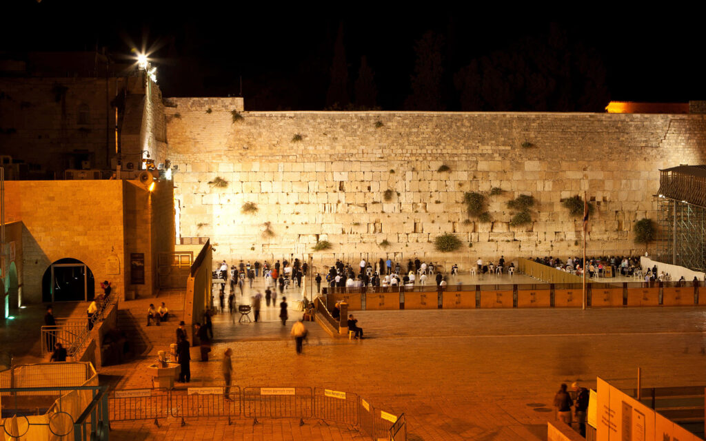 Western Wall Jerusalem illuminated at night with visitors reflecting against ancient stones wallpaper
