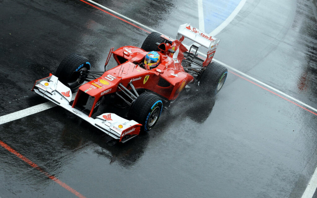 Drenched in Speed: Fernando Alonso Tackling a Rainy Race Circuit in his Red F1 Machine Wallpaper