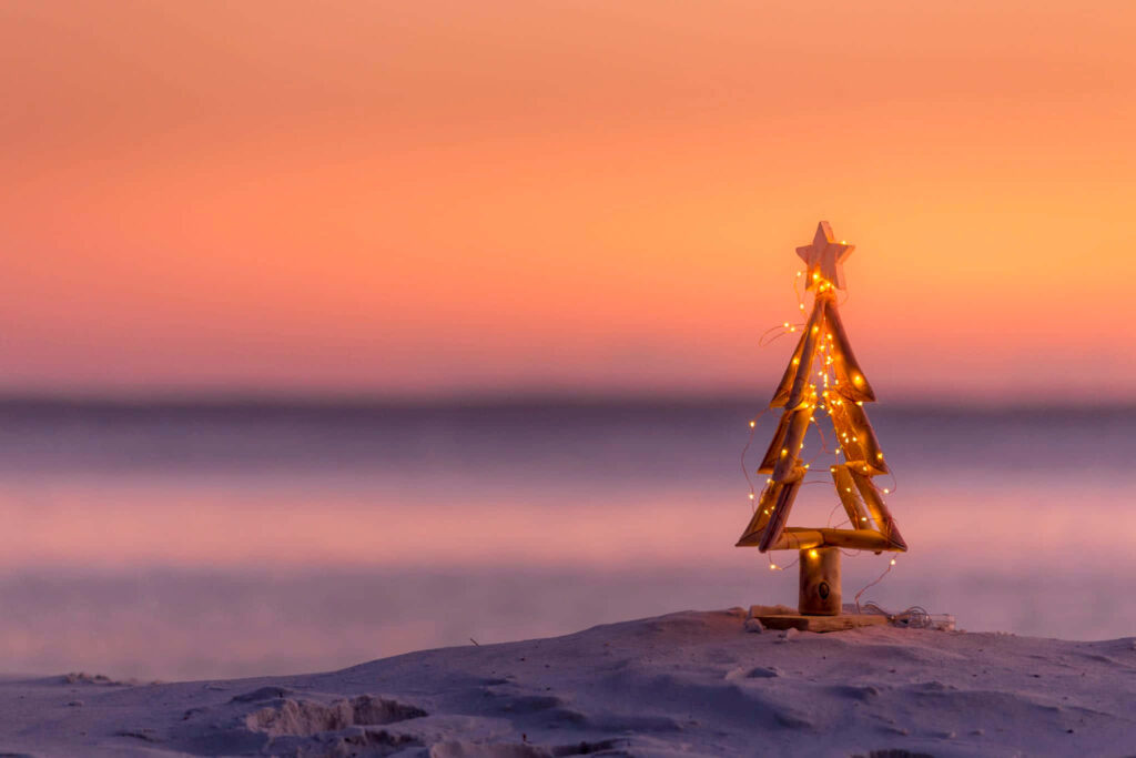 Whimsical Beach Sunset with Wooden Christmas Tree Lights Wallpaper