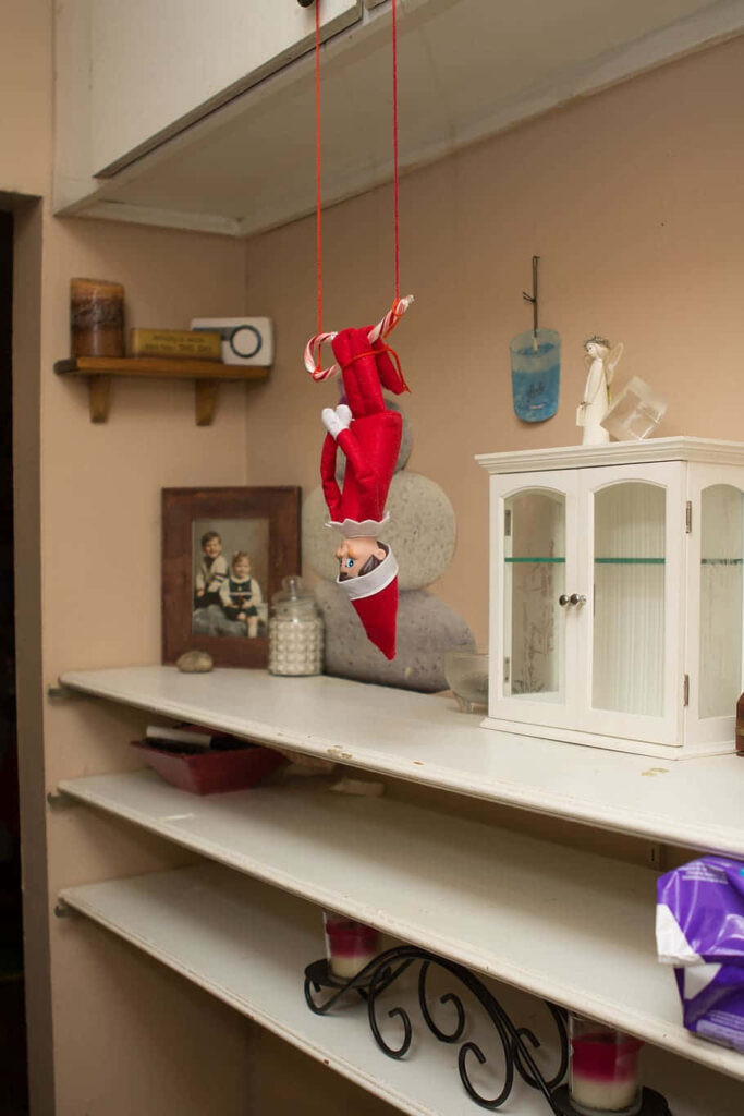 Whimsical Elf on the Shelf Hanging Upside Down in Cozy Room Wallpaper