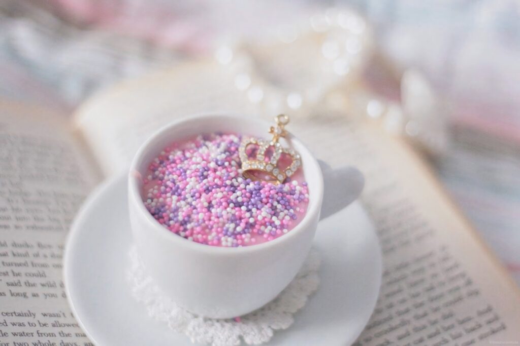 Delicate white teacup with pastel candy sprinkles and golden crown on lace doily background Wallpaper