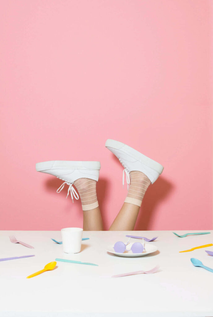 Playful Feet in White Sneakers Against Pastel Pink Wallpaper