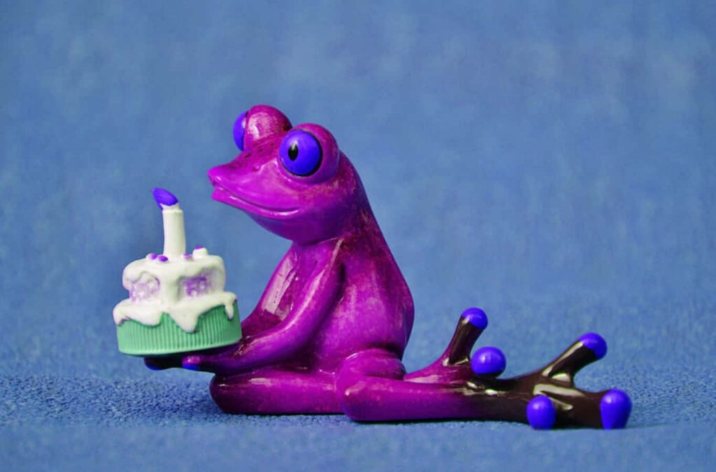 Playful Purple Frog with Birthday Cake on Textured Blue Background Wallpaper