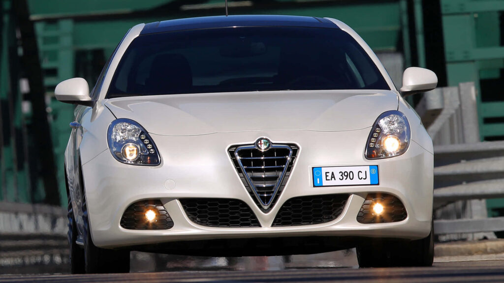White Alfa Romeo Giulietta driving on city street with sharp headlights and Italian design wallpaper