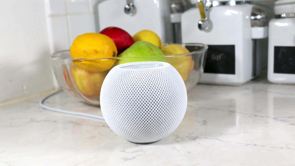 White Apple HomePod mini on marble countertop with blurred fresh fruit bowl in bright natural light Wallpaper