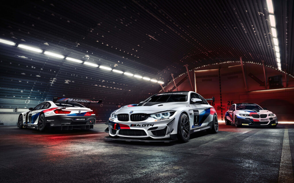 White BMW M4 GTS race car in modern garage flanked by two BMW race cars wallpaper background