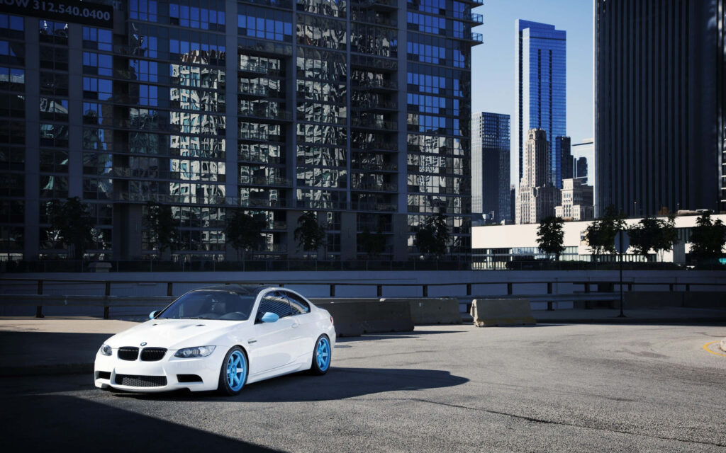 White BMW with blue rims parked on rooftop with modern city skyline in daylight wallpaper background