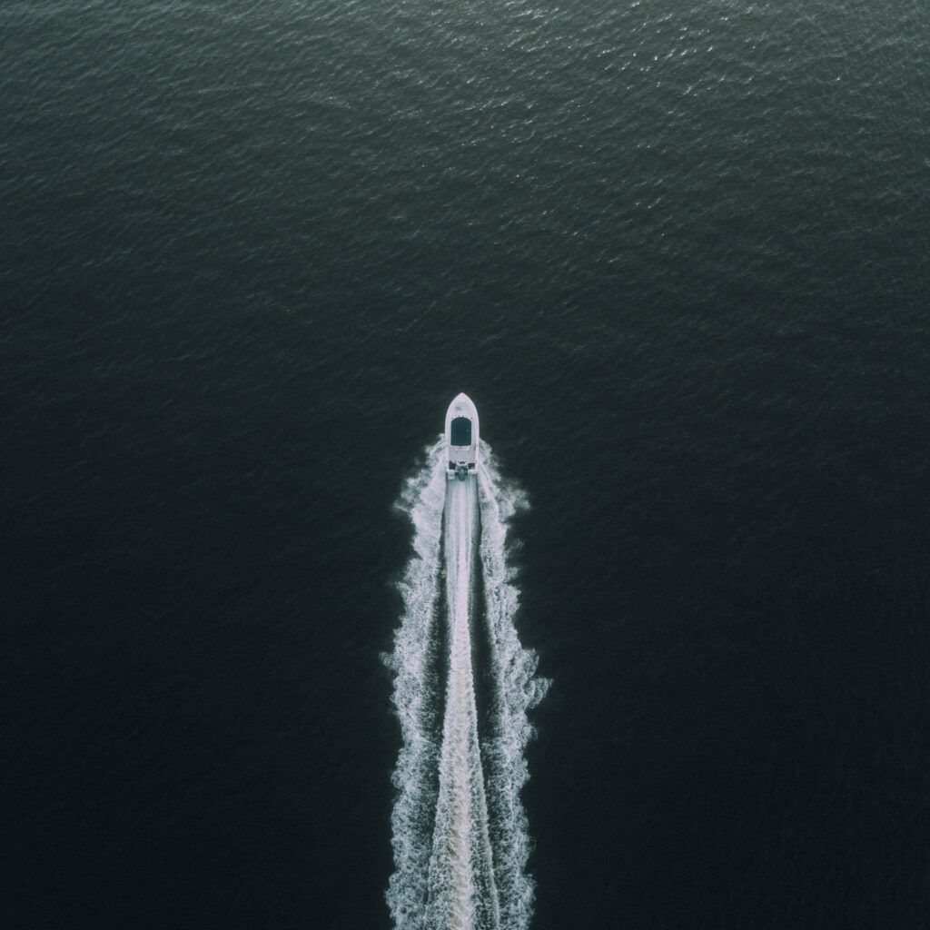 White boat sailing on calm expansive water with gentle wake scenic wallpaper background