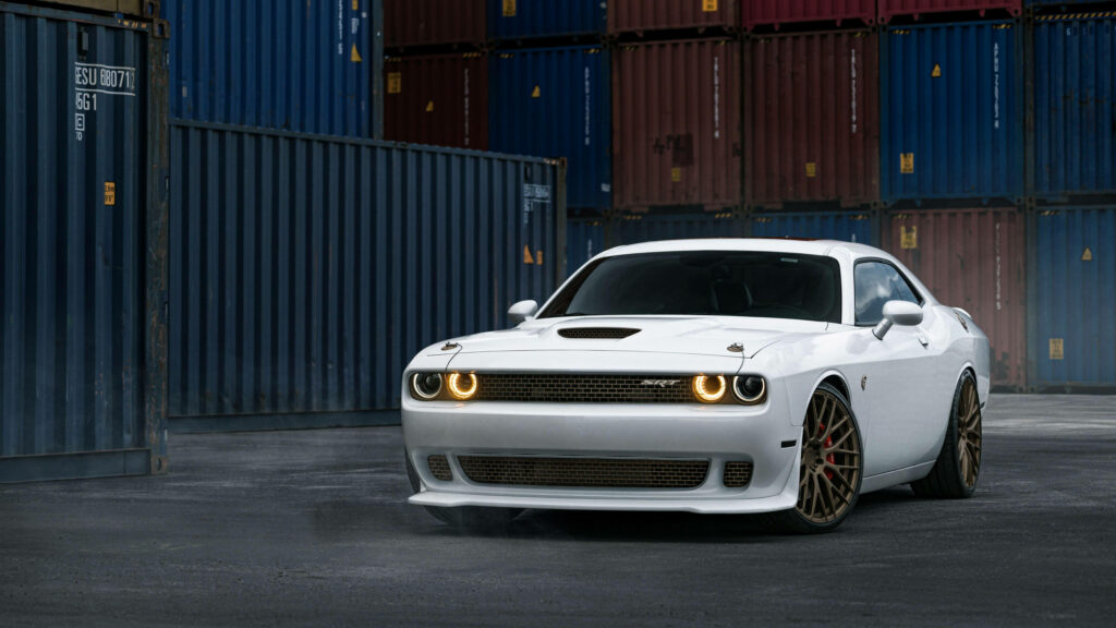 White Dodge Challenger Demon with glowing headlights parked by colorful shipping containers in 4K Wallpaper