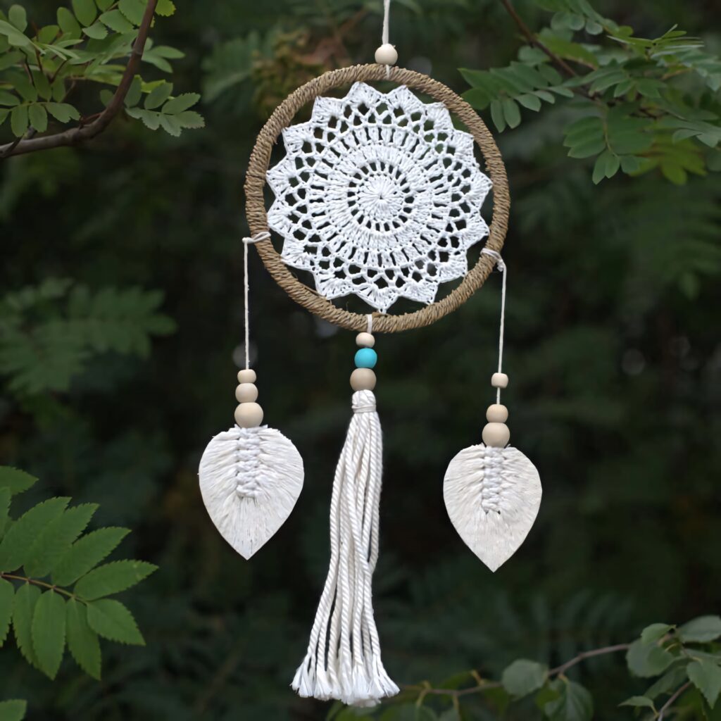 White dream catcher with crochet patterns wooden beads and tassels hanging on tree outdoors Wallpaper