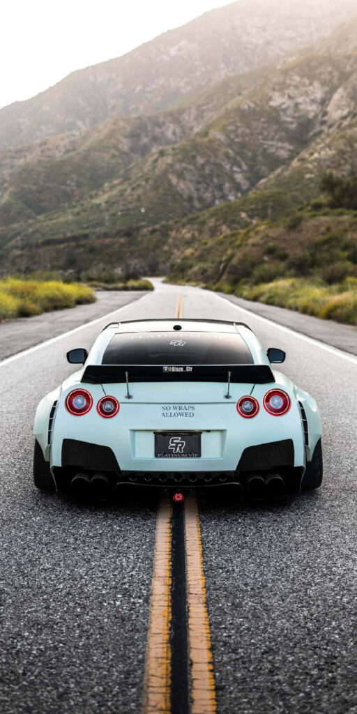 White GTR R35 parked on scenic mountain road with rugged hills and lush greenery background Wallpaper