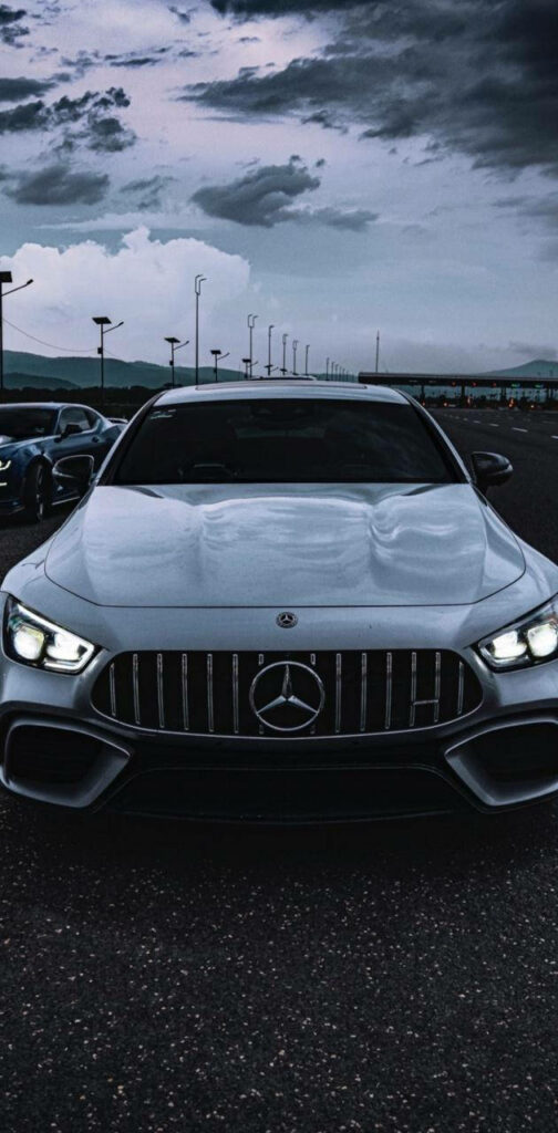 White Mercedes-AMG car with glowing headlights under dark stormy sky automotive wallpaper background
