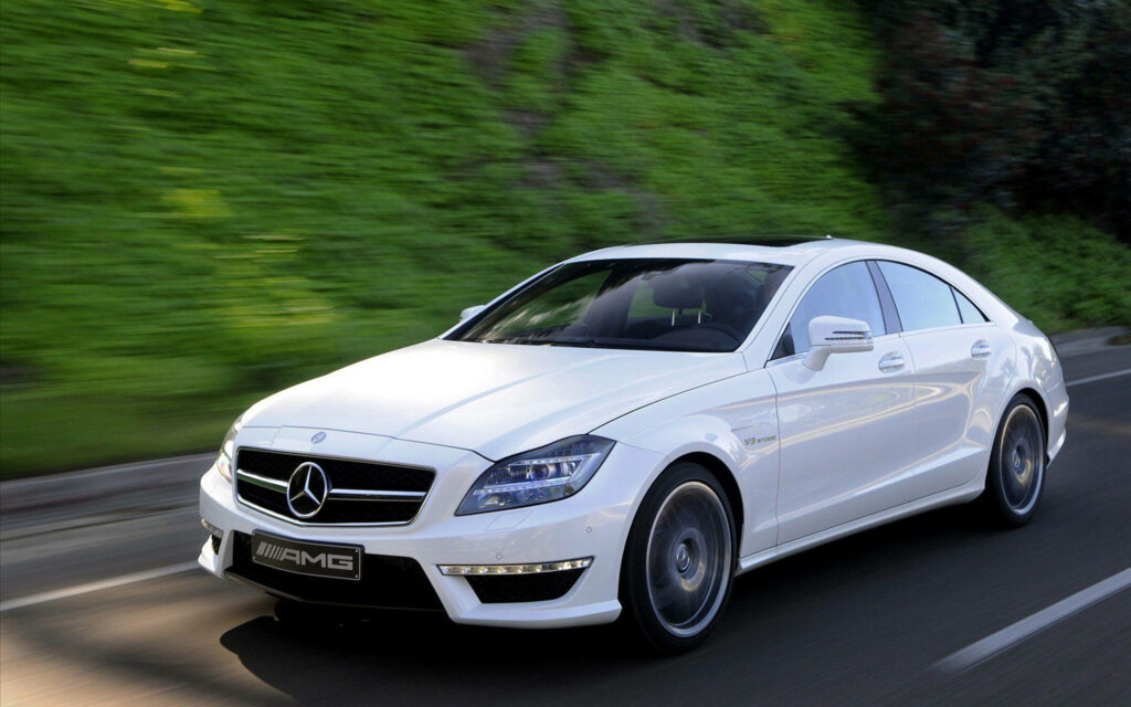 White Mercedes-Benz AMG CLS63 driving on open road with lush green background in high definition Wallpaper