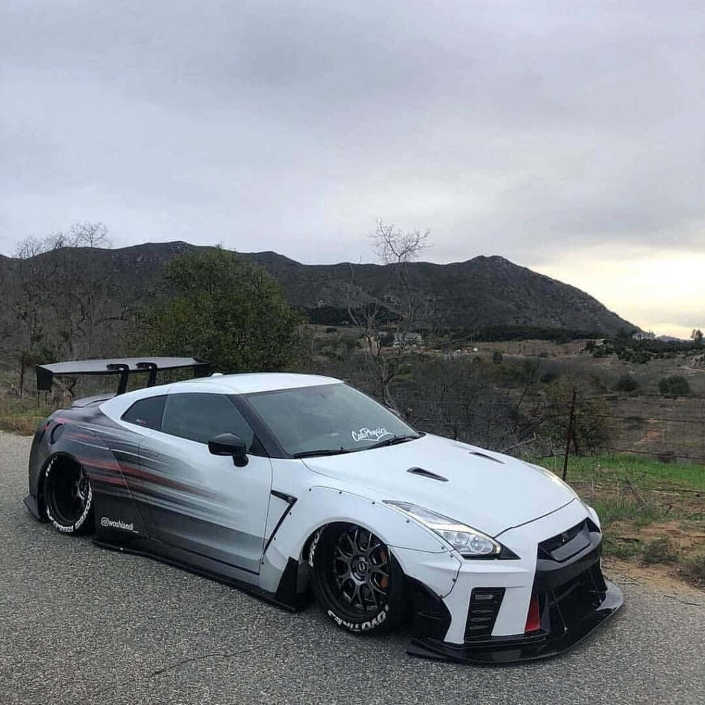 White Nissan R35 GTR with custom body kit parked on mountain road with hills and cloudy sky Wallpaper