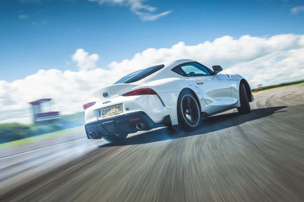 White Toyota Supra drifting on racetrack under blue sky showcasing sporty design and performance Wallpaper