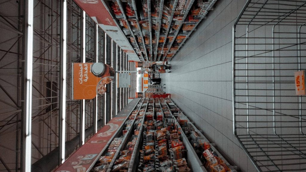 Wide grocery store aisle wallpaper low-angle with symmetrical shelves and bright lighting background