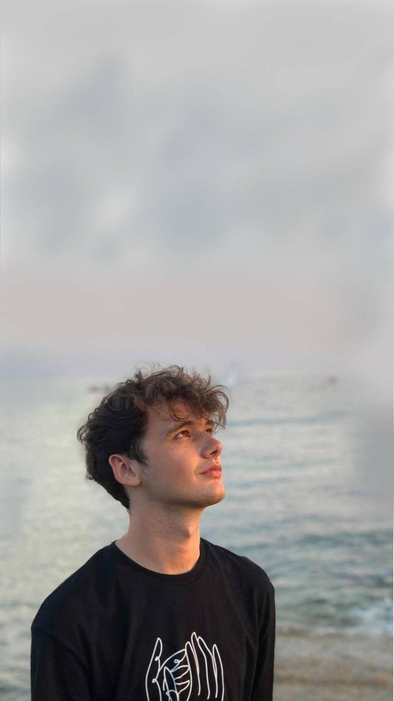 Wilbur Soot thoughtful portrait in black tee on serene beach with warm natural lighting wallpaper