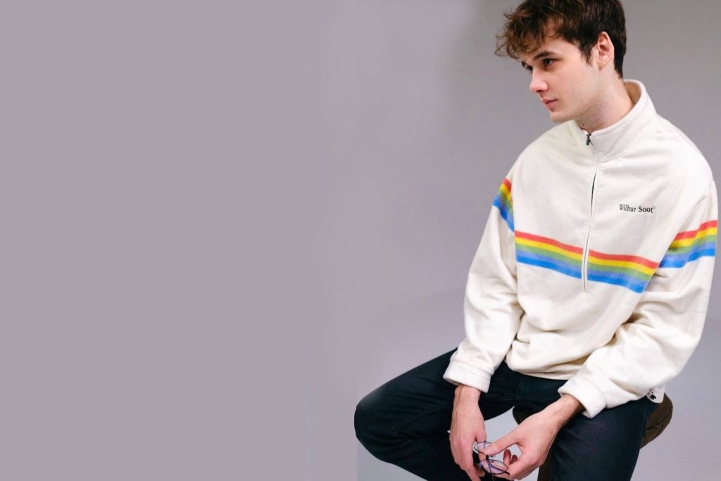 Wilbur Soot in white rainbow-striped fleece jacket studio portrait against grey background Wallpaper