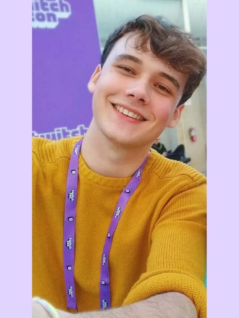 Wilbur Soot smiling in yellow sweater with TwitchCon lanyard vibrant candid portrait wallpaper