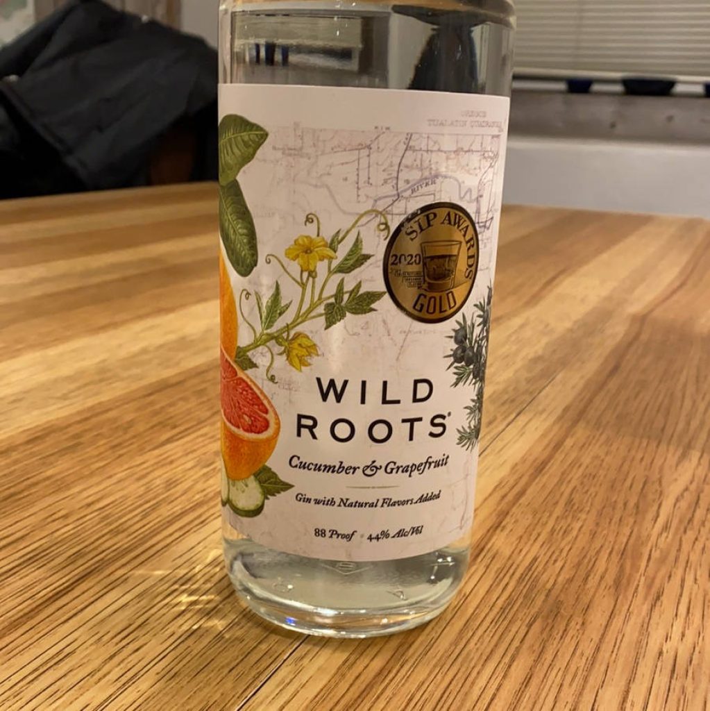 Wild Roots Cucumber Grapefruit Gin bottle with botanical label and 2020 SIP Gold medal on wood table Wallpaper