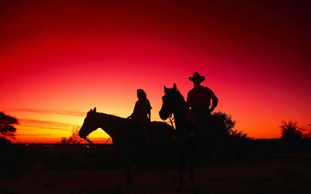 Cowboy riding wild horse at vivid sunset in American desert wild west landscape wallpaper