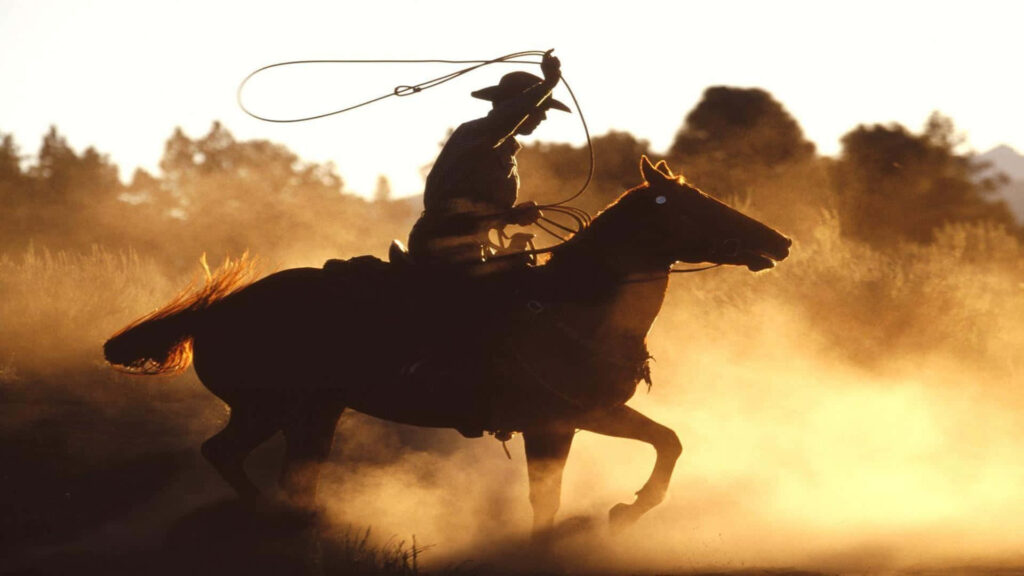 Silhouette of cowboy on horseback at golden sunset with swirling dust wild west adventure wallpaper