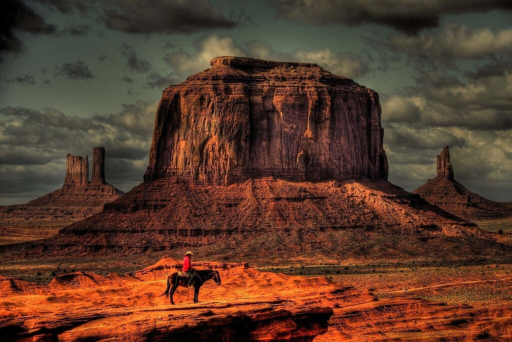Cowboys riding horses through rugged red rock canyon landscape under dramatic sky Wild West Wallpaper