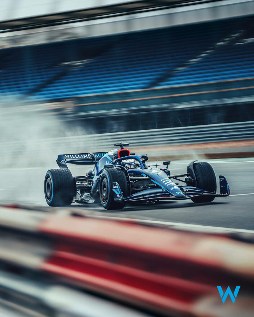 Williams Formula 1 car speeding on empty racetrack with tire smoke and sleek blue design Wallpaper