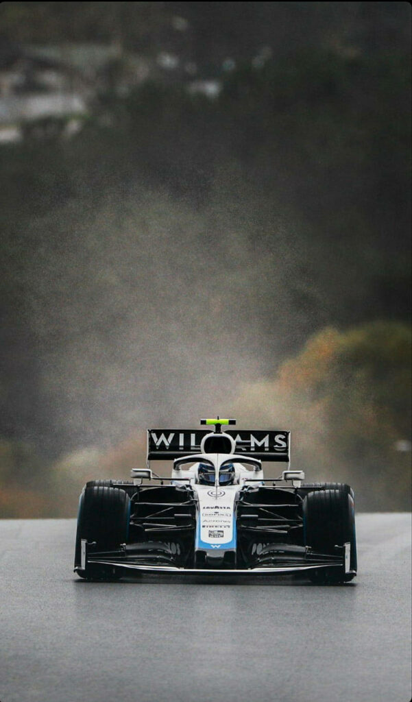 Williams Racing car racing on wet track through misty forest capturing intense motorsport action Wallpaper