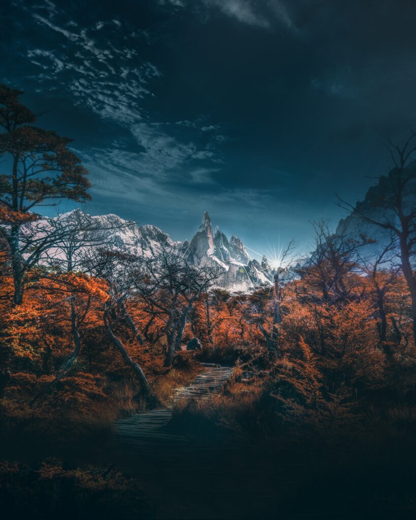 Winding path through vibrant autumn forest leading to snow-capped mountains under blue sky Wallpaper