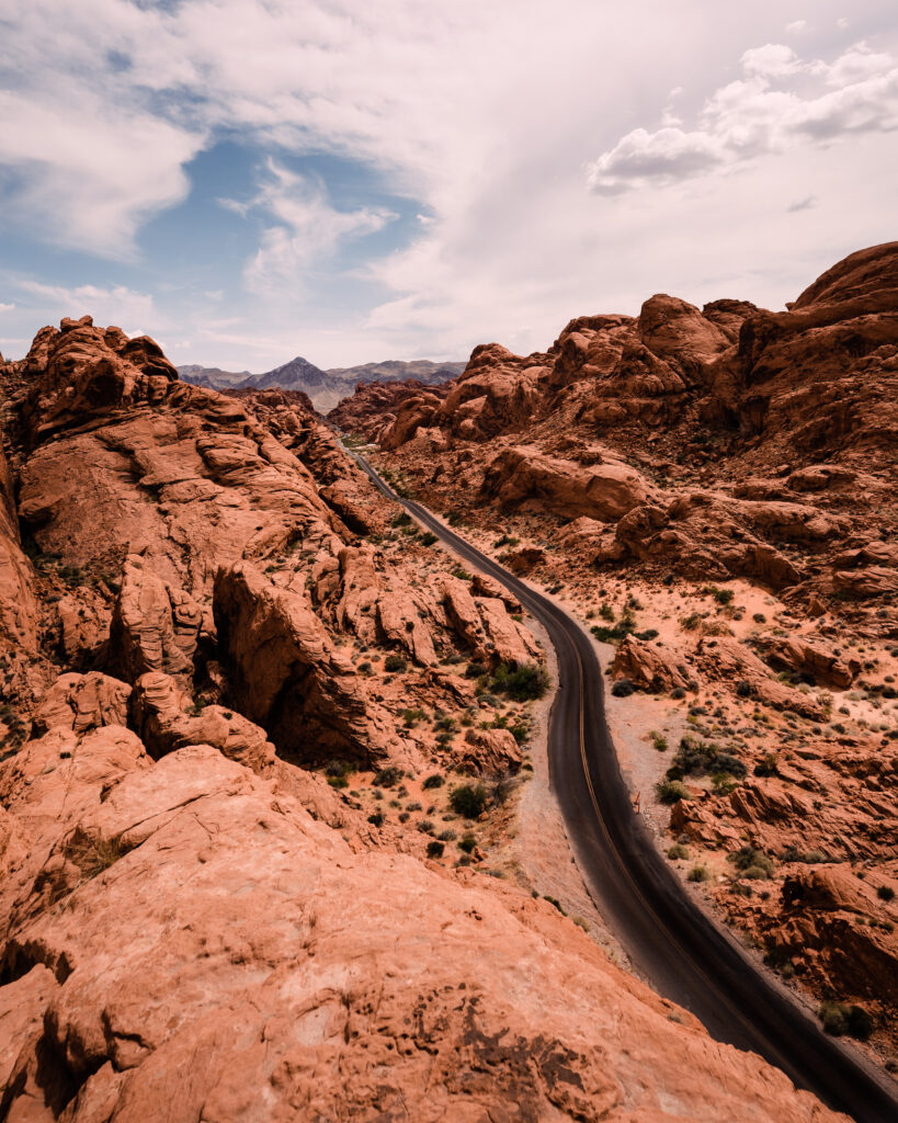 Aerial view of winding road through red rock canyon with desert plants under cloudy sky wallpaper