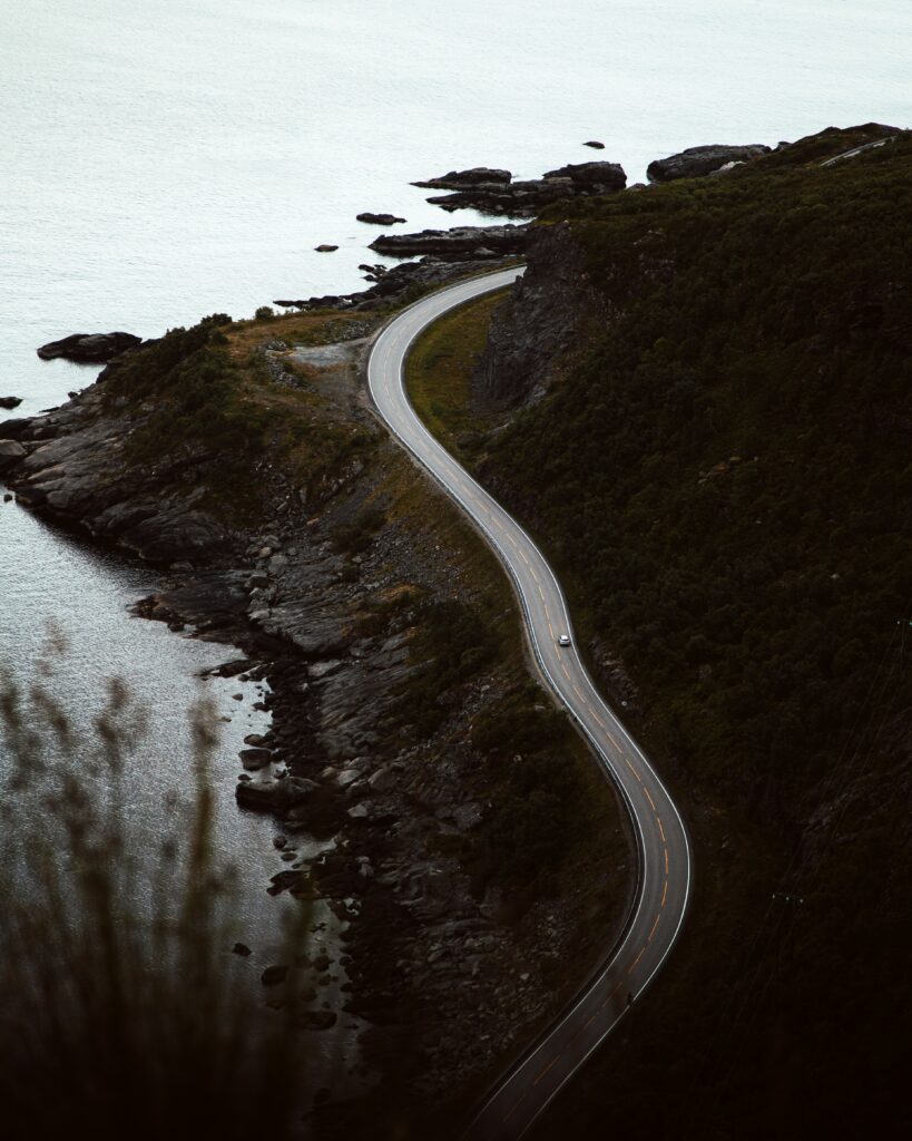 Aerial view of winding coastal road with dark rocks and calm sea in moody natural tones wallpaper