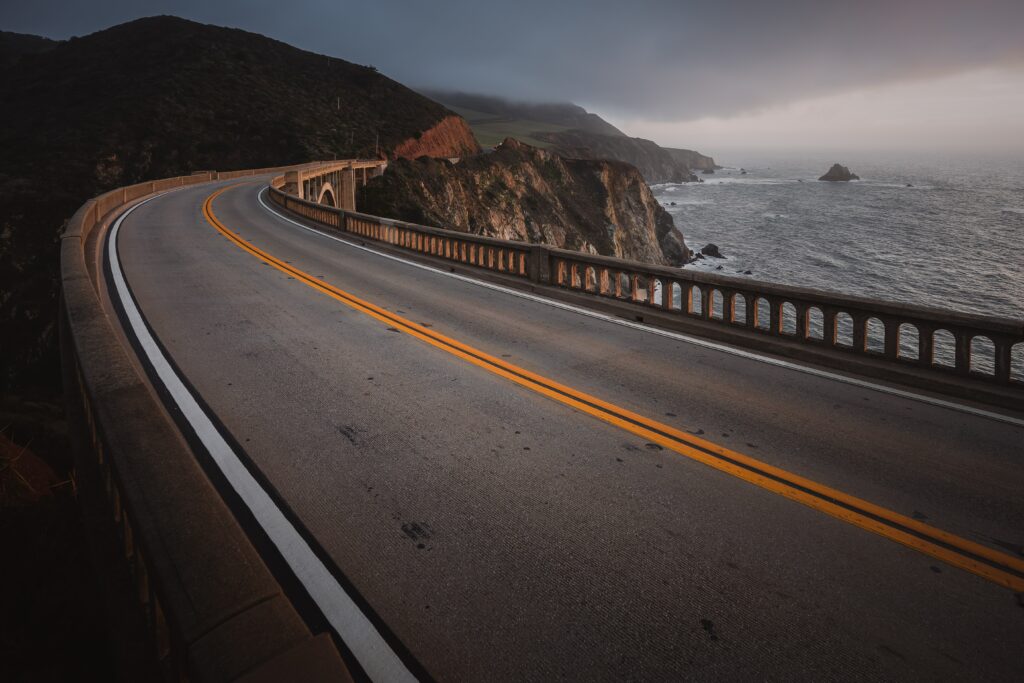 Winding asphalt road along rugged coastal cliffs with rocky terrain and dramatic ocean views Wallpaper