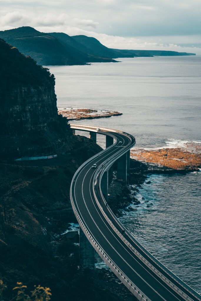 Winding coastal road curves above rocky cliffs along deep blue ocean with serene natural beauty Wallpaper