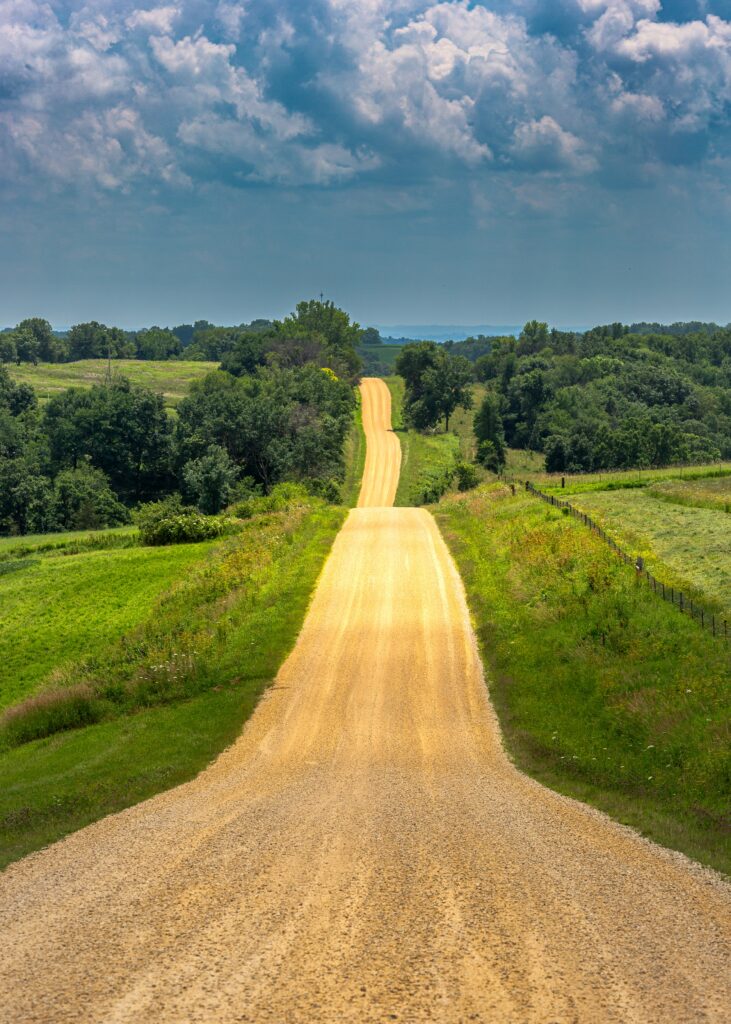 Winding country road through green hills under dramatic cloudy sky scenic nature background Wallpaper