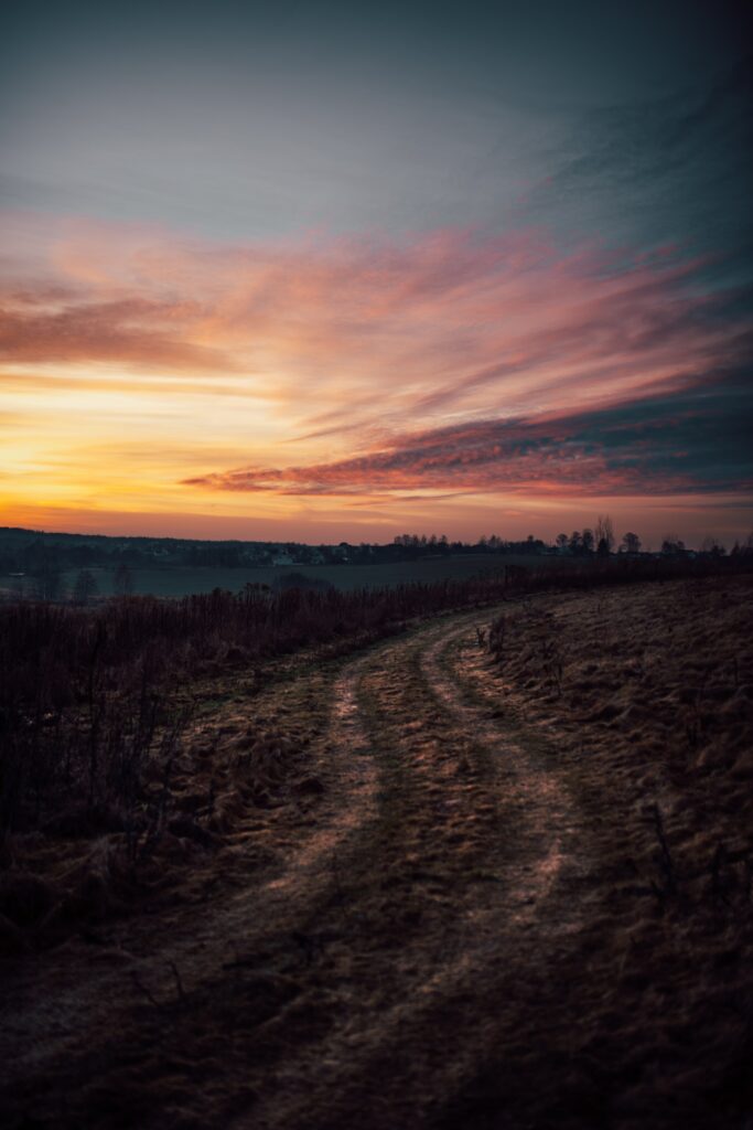 Winding country road through open fields under vibrant twilight sky with sunset hues wallpaper