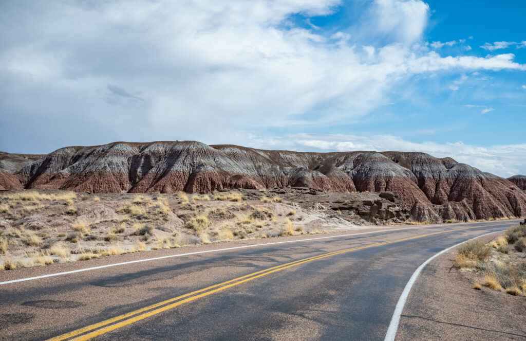 Winding desert road through rugged hills and layered mountains under a bright blue sky wallpaper