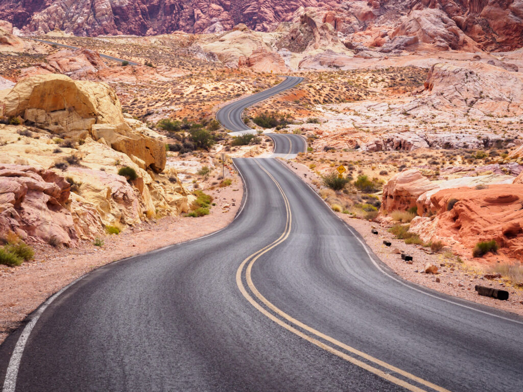 Winding asphalt road through red and orange desert rocks under a clear expansive sky wallpaper