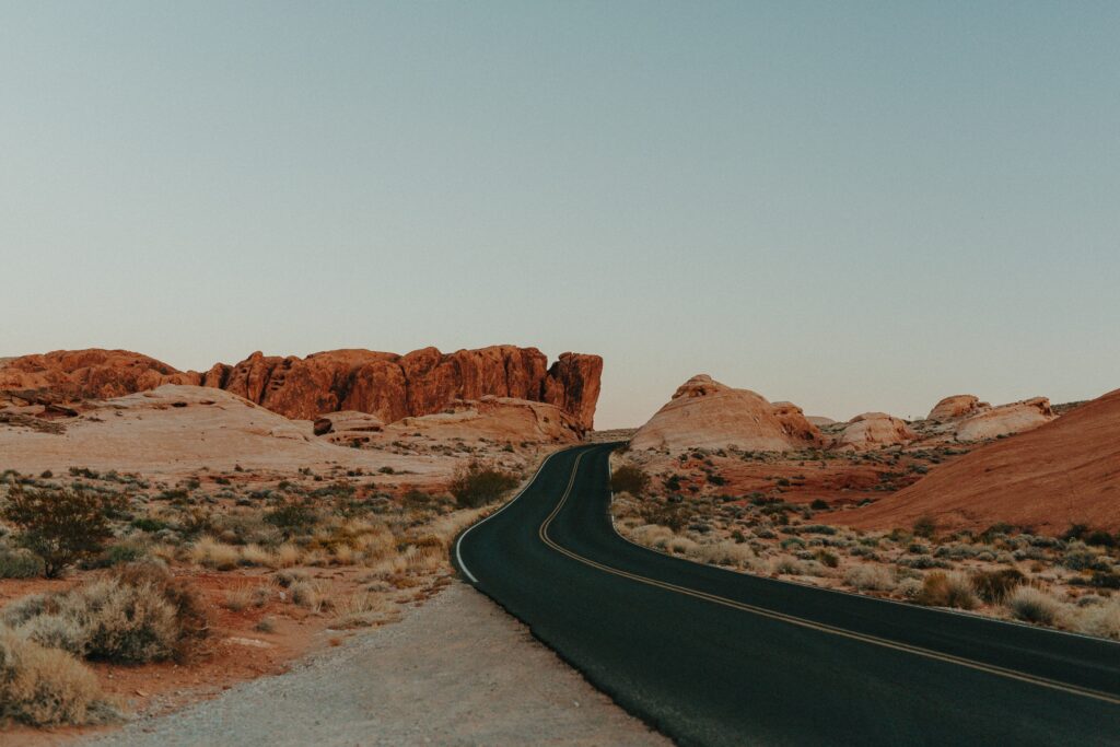 Winding desert road with stone formations and sparse vegetation under soft blue sky wallpaper