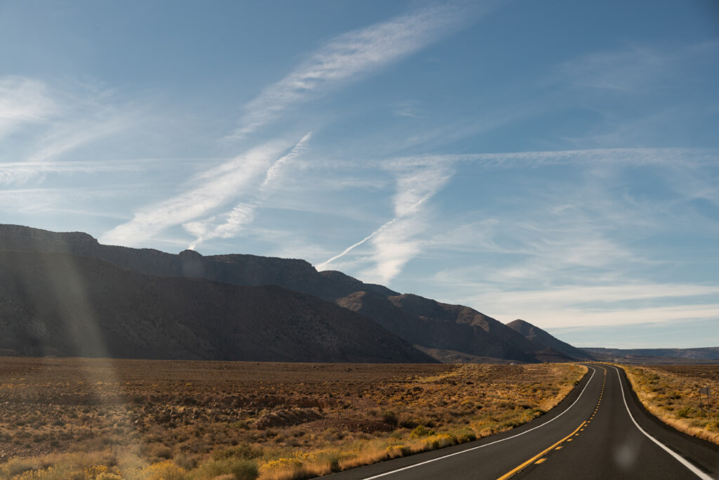 Winding desert road with rugged mountains and blue sky with wispy clouds wallpaper background