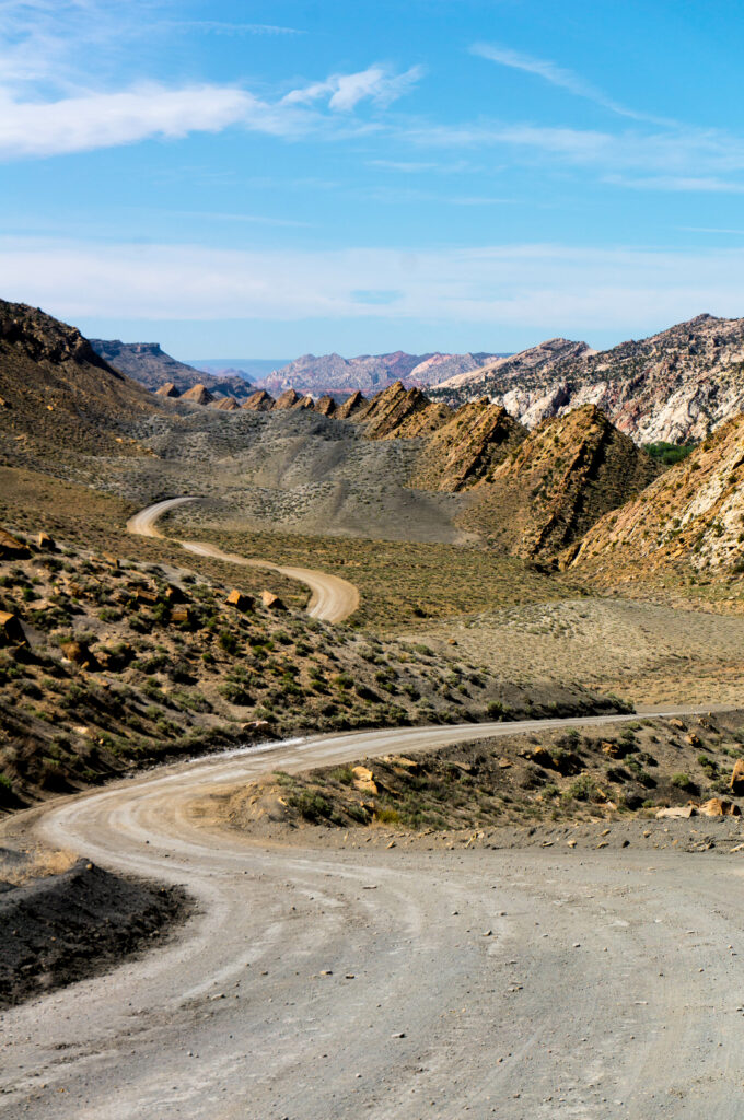 Winding dirt road through rugged hills and rocky mountains under bright blue sky scenery Wallpaper