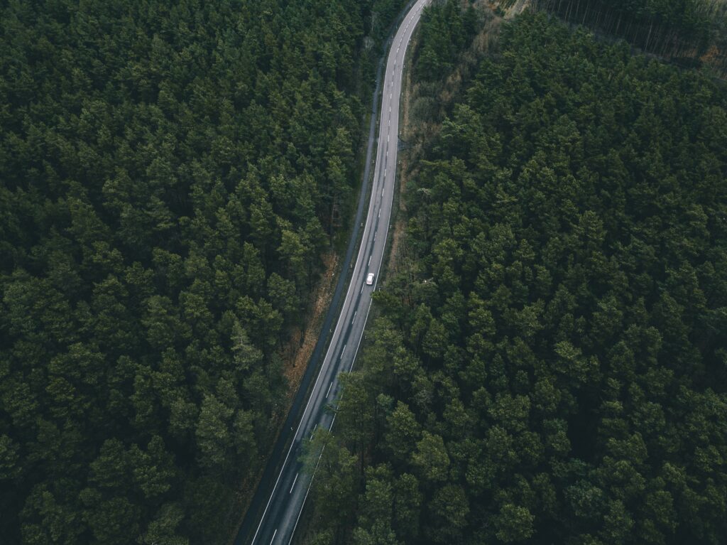 Aerial view of winding road through dense green forest with car showcasing nature's beauty Wallpaper